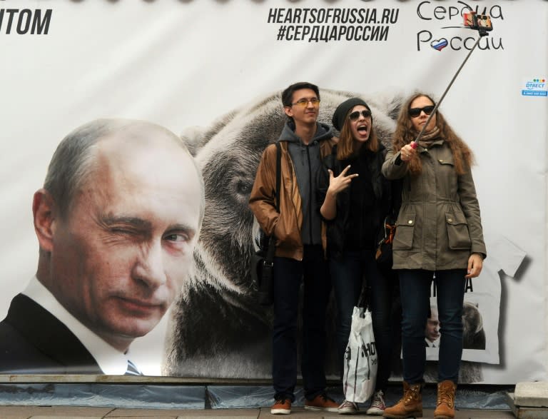 People posing for a selfie photograph in front of a banner depicting Russian President Vladimir Putin in St. Petersburg