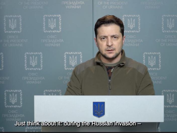 President Volodymyr Zelensky in a video address released February 28, 2022. He is at a podium with a Ukrainian flag nearby.