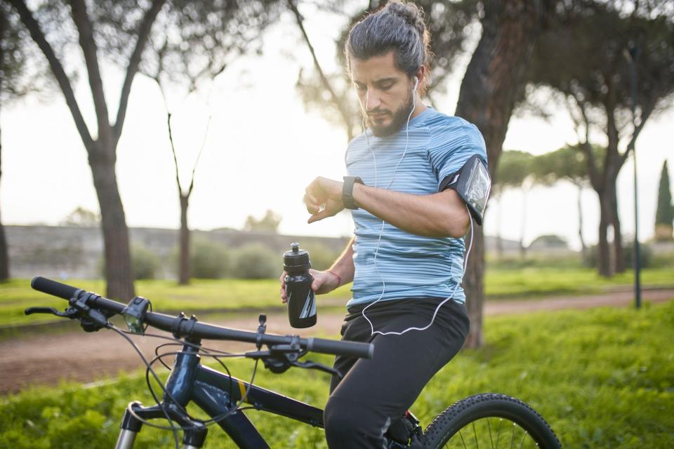 A man checking on smartwatch while riding a bicycle through a park