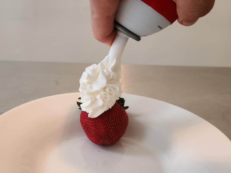hand spraying can of dairystar whipped cream onto a strawberry