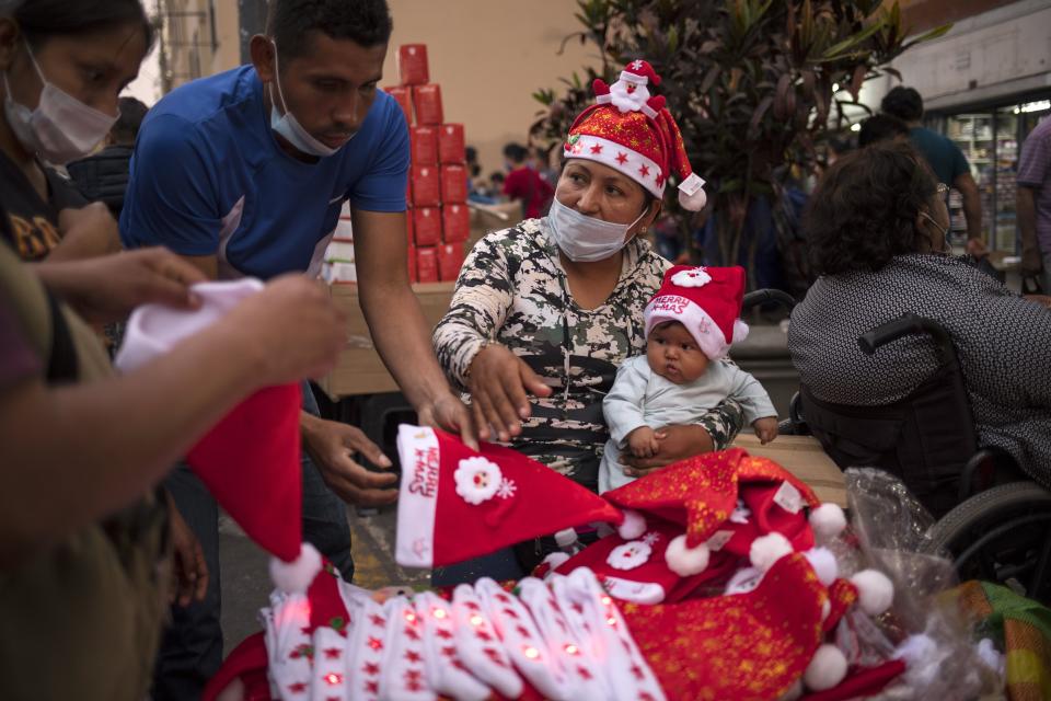 A woman sells Santa Claus hats while holding her baby at the Mesa Redonda Market, a popular spot for Christmas shopping, amid the COVID-19 pandemic in Lima, Peru, Monday, Dec. 21, 2020. (AP Photo/Rodrigo Abd)