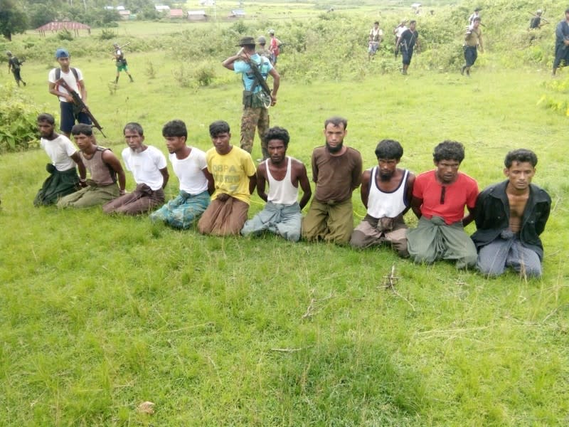 Ten Rohingya men with their hands bound kneel as members of the Myanmar security forces stand guard in Inn Din village