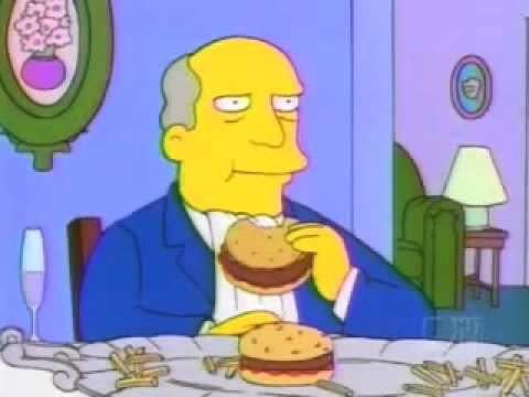 Superintendant Chalmers sits at a table, a platter of burgers and fries in front of him, he's taking a bite