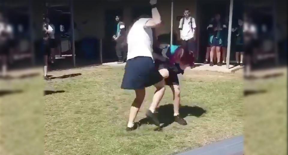 A screenshot from a video shows and older student punching a cowering younger student at Calamvale Community College. 