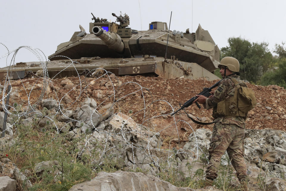 A Lebanese soldier stands in front of a Israeli Merkava tank in the disputed Kfar Chouba hills along the border, in south Lebanon, Friday, June 9, 2023. Israeli soldiers fired tear gas to disperse scores of protesters who pelted the troops with stones along the border with Lebanon Friday, leaving some Lebanese demonstrators and troops suffering breathing problems. (AP Photo/Mohammad Zaatari)