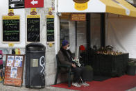 A lottery seller wearing a face mask sits outside a butcher in Lisbon, Monday, Nov. 29, 2021. Portuguese health authorities on Monday identified 13 cases of omicron, the new coronavirus variant spreading fast globally, among members of the Lisbon-based Belenenses SAD soccer club, and were investigating possible local transmission of the virus outside of southern Africa. (AP Photo/Ana Brigida)