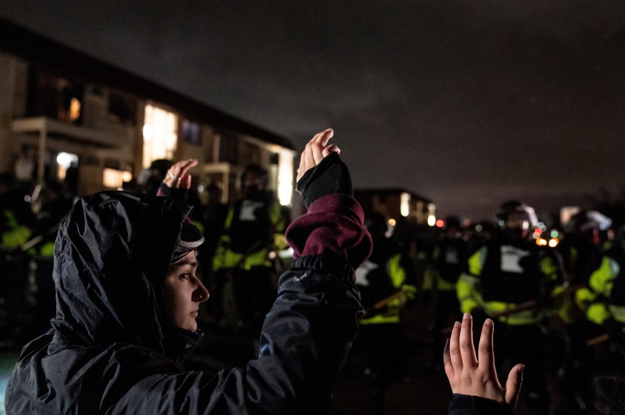 Demonstrators raise their hands while facing off against a perimeter of police as they defy an order to disperse during a protest against the police shooting of Daunte Wright, Monday, April 12, 2021, in Brooklyn Center, Minn.