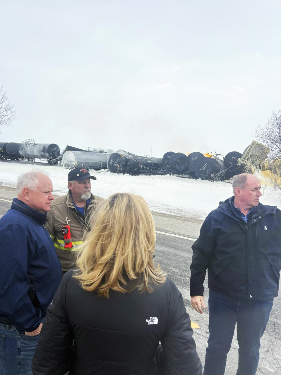 In this photo provided by the office of Minnesota Gov. Tim Walz, Walz visits the site of a fiery train derailment on Thursday, March 30, 2023, in Raymond, Minn. The early morning derailment spilled ethanol, which caught fire and prompted residents within a half-mile radius of the incident to evacuate. Walz, far left, stands next to Raymond Mayor and Assistant Fire Chief Ardell Tensen. Also pictured is Matt Igoe, executive vice president and COO of BNSF Railway, and Katie Farmer, chief executive officer of BNSF Railway. (Teddy Tschann/Office of Minnesota Gov. Tim Walz via AP)