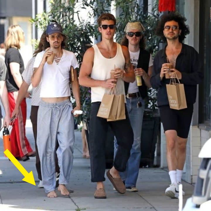 Shawn and three friends, one of whom is barefoot, walking down a sidewalk while sipping on smoothies