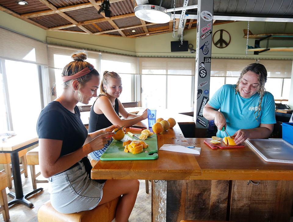 Sarah Bowe and Catherine Daoulas, both 17, help bartender Jaylynn Hurd, 25, slice oranges for the bar at The Jetty restaurant in the Brant Rock Beach neighborhood of Marshfield on Thursday, Aug. 19, 2021.