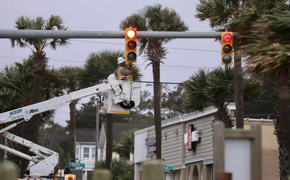 An electrical crewman works on a traffic signal as strong winds whip palm trees overhead as a severe storm approaches North Myrtle Beach S.C. on Tuesday morning. Jan. 9, 2024