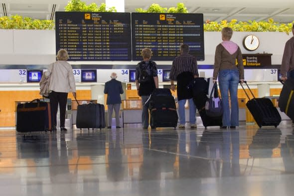 A7BPPF Airport passengers with luggage standing waiting at check in area on concourse looking at flight information boards