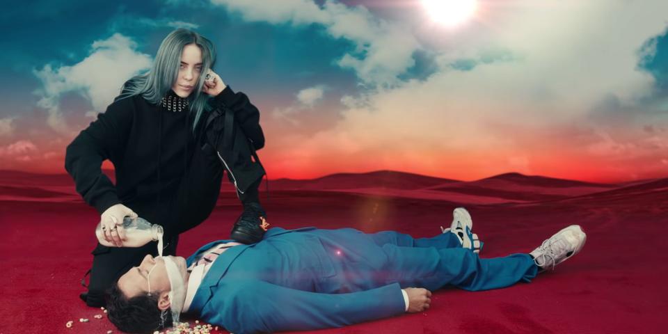 Billie Eilish pouring milk into the mouth of a man lying on the ground.