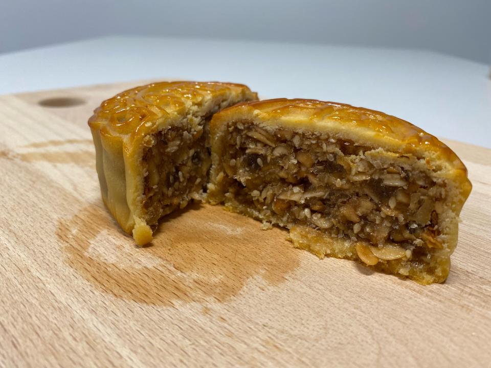 A mixed nuts mooncake cut in half. The mixed nuts mooncake has walnuts, pumpkin seeds, oats, dried fruit, golden syrup and sesame seeds.