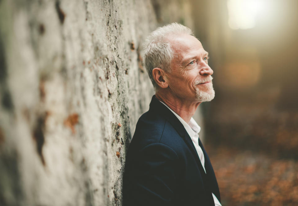 Older man with gray hair leaning against a tree