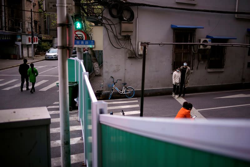 People wearing face masks walk at a residential area blocked by barriers in Wuhan