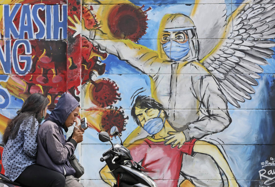 A motorist stops to light up a cigarette near a mural honoring honoring health care workers during the new coronavirus outbreak on the outskirts of Jakarta, Indonesia, Tuesday, June 2, 2020. (AP Photo/Dita Alangkara)