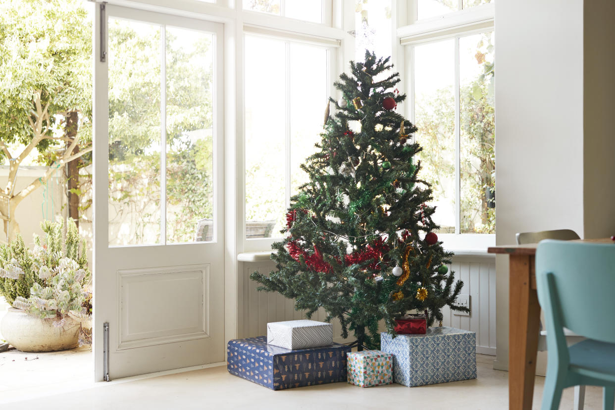 Christmas tree with gift boxes by window at entrance of house