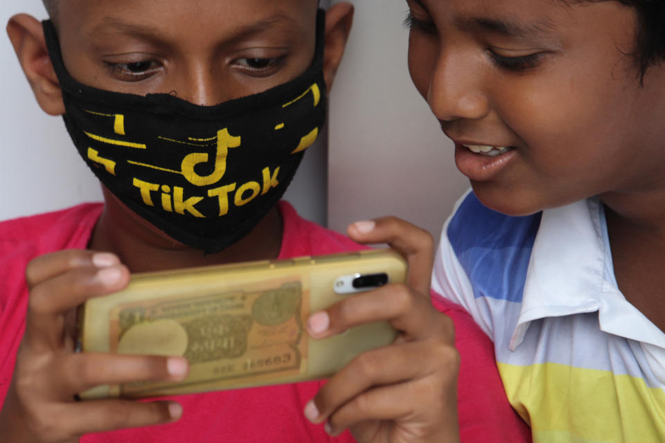 A boy wearing a face mask with the TikTok logo uses a mobile phone outside the downed shutters of a shop in Mumbai, India on July 29, 2020. Photo: Himanshu Bhatt/NurPhoto/Getty