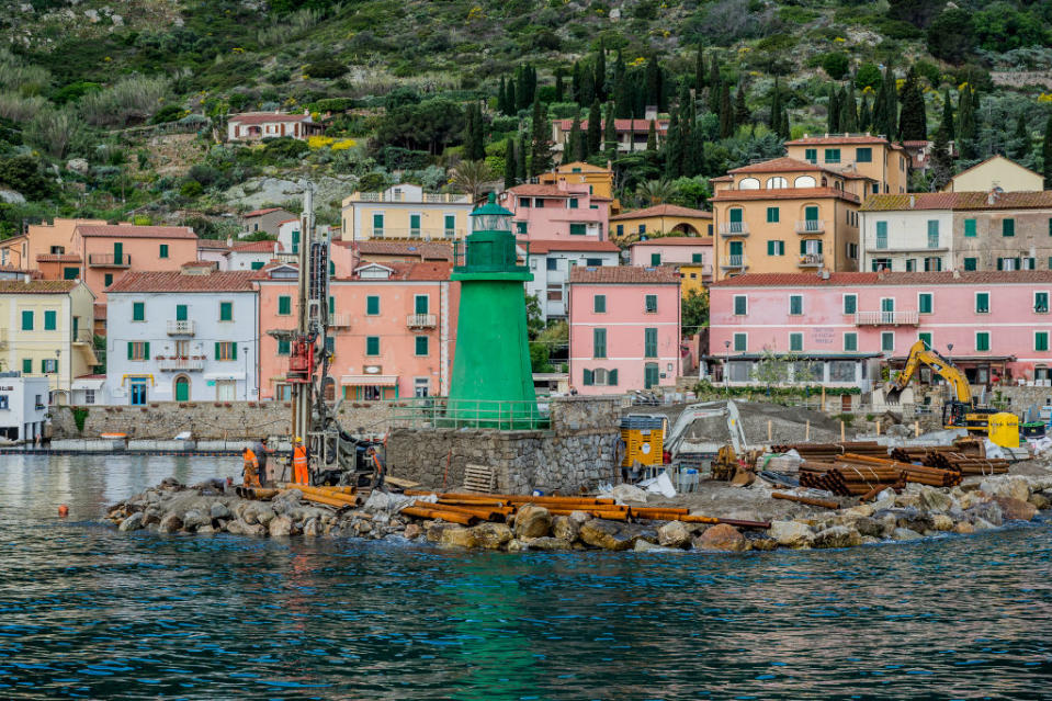 Pictured are colourful houses and a green lighthouse on the coast of Giglio.