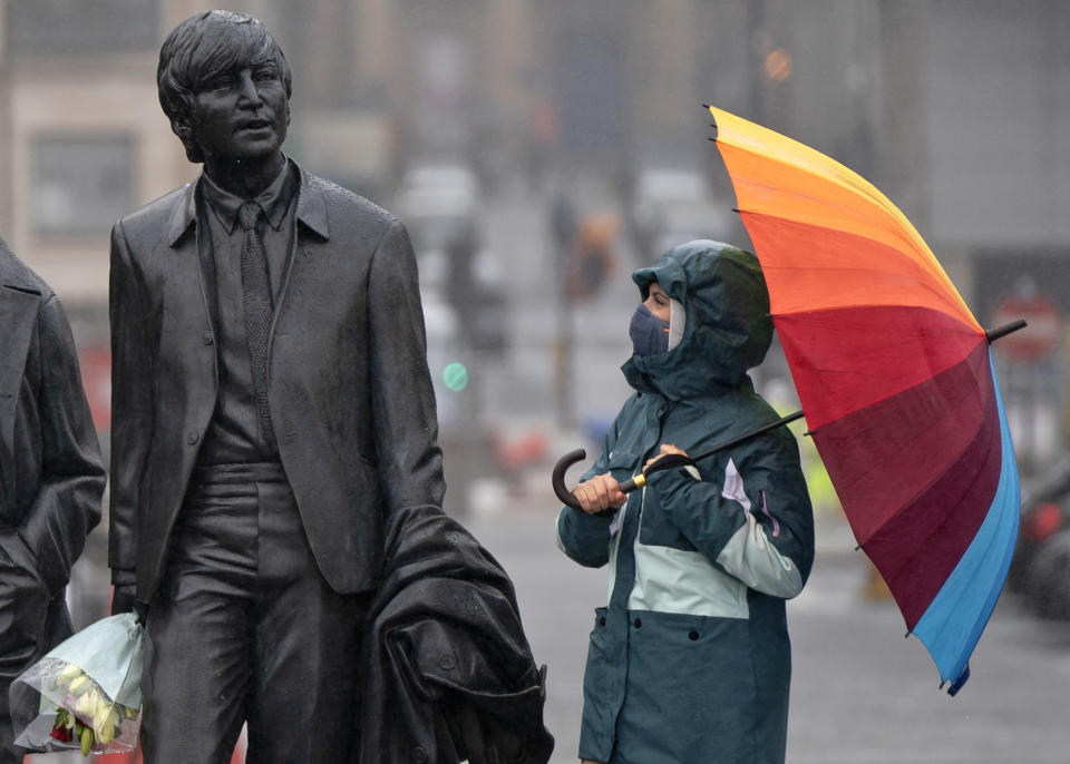 A youth wearing a face mask looks up at statue of John Lennon, part of a larger statue of The Beatles in Liverpool, England, Monday Oct. 12, 2020, as Prime Minister Boris Johnson prepares to lay out a new three-tier alert system for England. The Liverpool City Region is expected to face the tightest restrictions under the new system, which will classify regions as being on "medium", "high" or "very high" alert. (AP Photo/Jon Super)