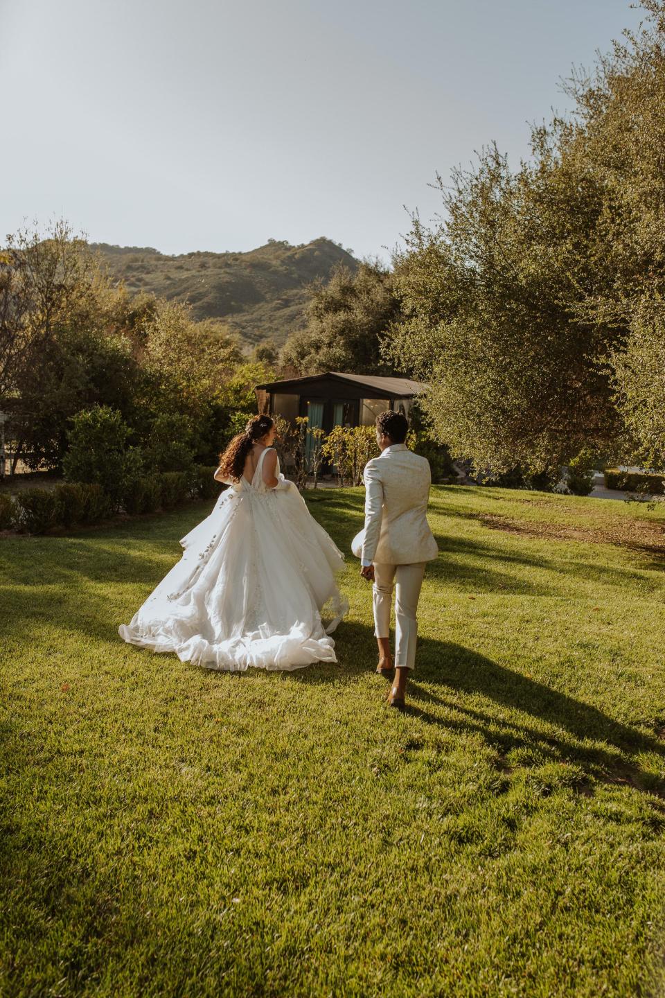 A bride and groom run through a field.