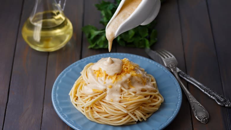 pouring creamy sauce on pasta