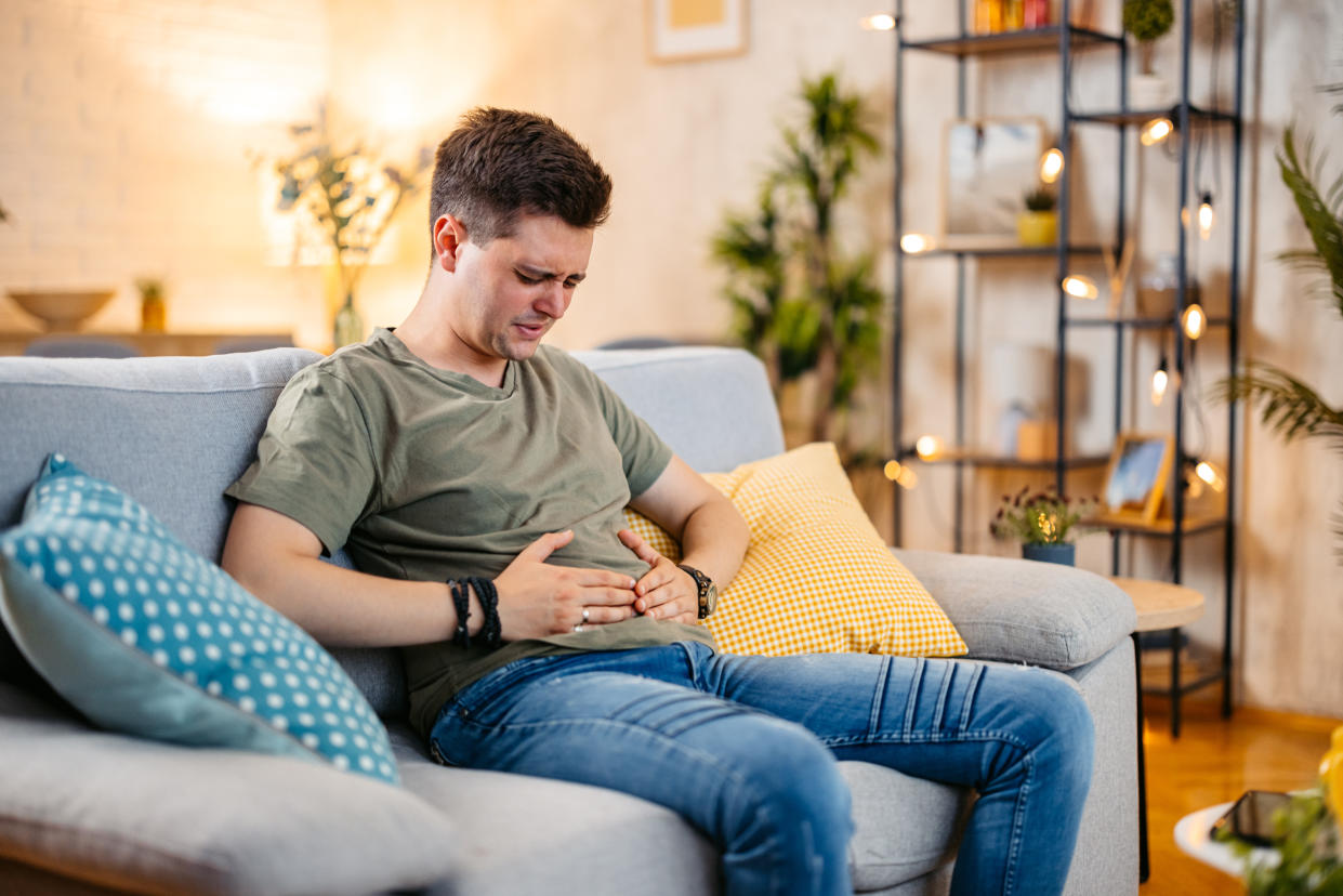 Young having stomach pain while sitting on the sofa at home.