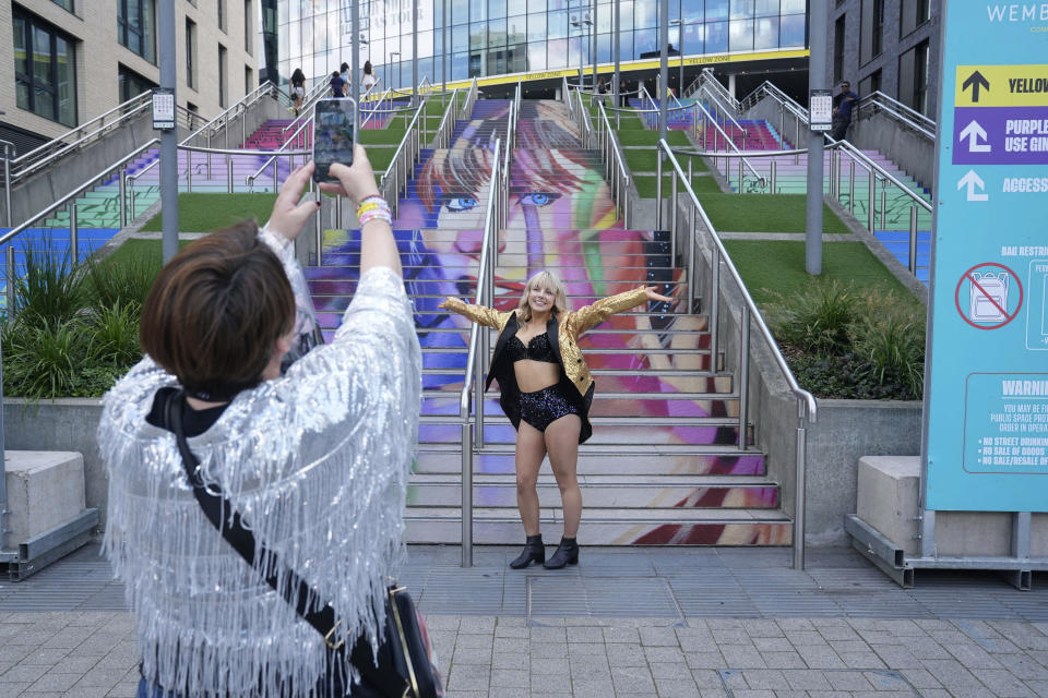 A fan poses for a photo by a staircase with the image of Taylor Swift, outside Wembley Stadium ahead of her first London concert, during the Eras Tour, in London, Friday June 21, 2024. (Lucy North/PA via AP)