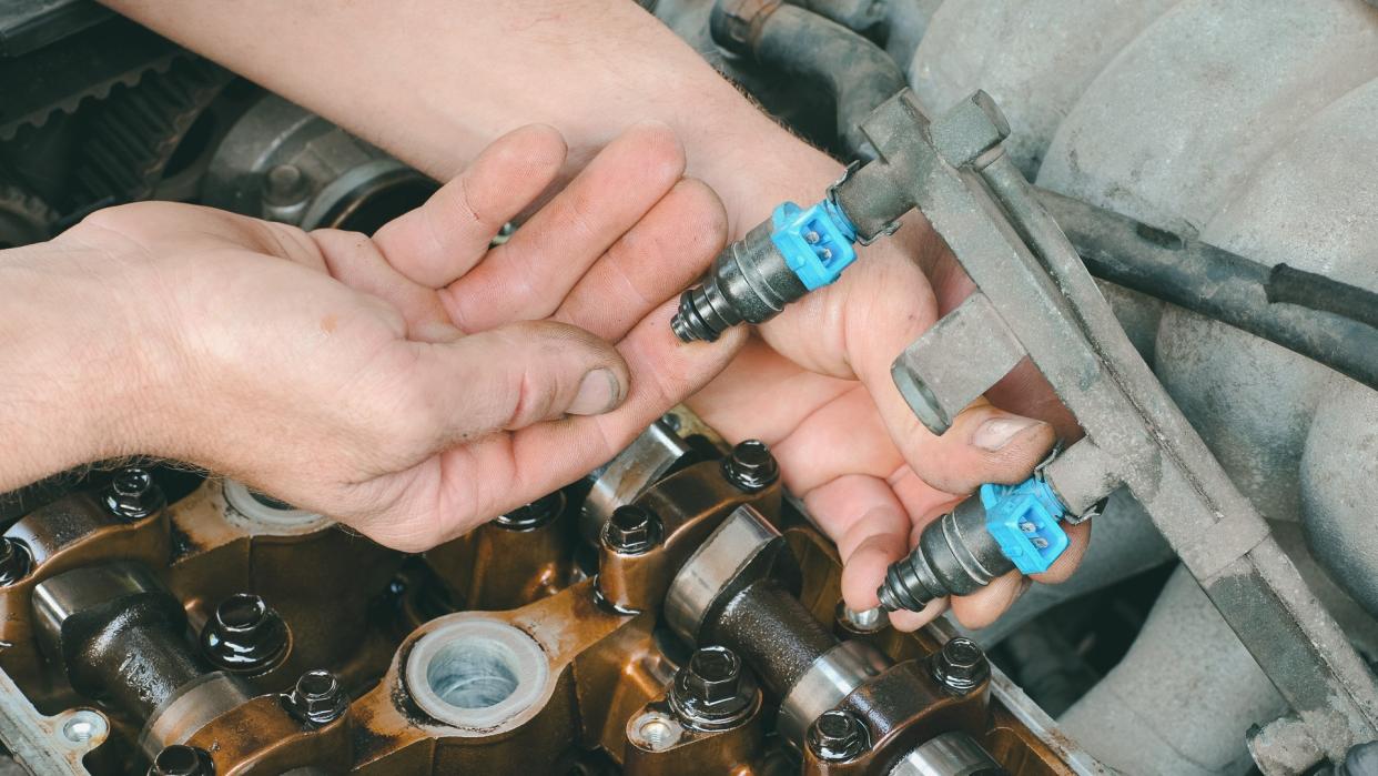 Car mechanic fixing fuel injector at  two camshaft gasoline engine.