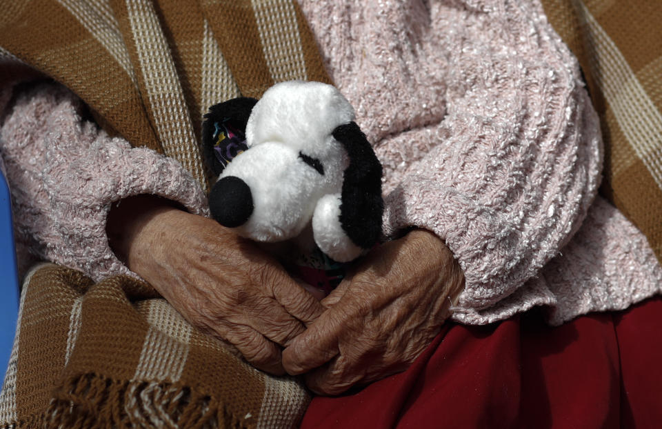 Una mujer sostiene a su perro de peluche Snoopy mientras espera su turno para una inyección de la vacuna Sinopharm COVID-19 en el hogar de ancianos de San Ramón durante el inicio de las vacunas para personas mayores de 80 años en La Paz, Bolivia, el lunes 5 de abril del 2021. (Foto AP/Juan Karita)