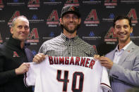 Newly acquired Arizona Diamondbacks pitcher Madison Bumgarner, center, holds his new jersey with general manager Mike Hazen, right, and manager Tory Lovullo during a team availability, Tuesday, Dec. 17, 2019, in Phoenix. (AP Photo/Matt York)