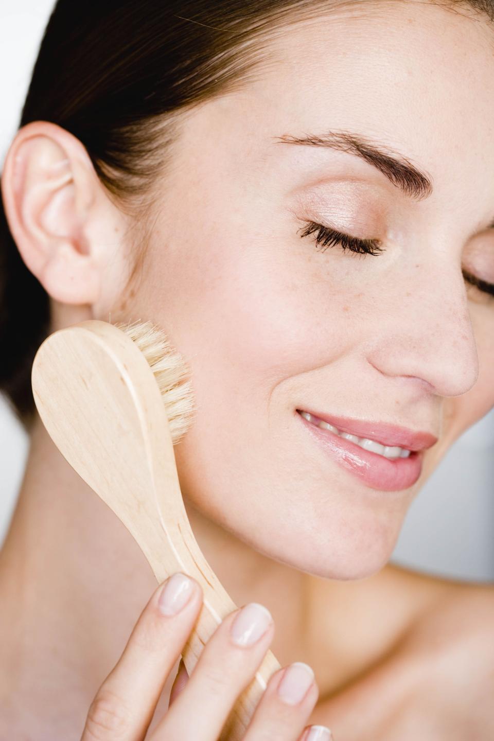 Woman dry brushing her face with eyes closed.