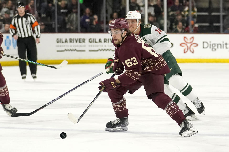 Arizona Coyotes' Matias Maccelli (63) brings the puck up ice against Minnesota Wild's Joel Eriksson Ek (14) during the first period of an NHL hockey game Wednesday, Feb. 14, 2024, in Tempe, Ariz. (AP Photo/Darryl Webb)