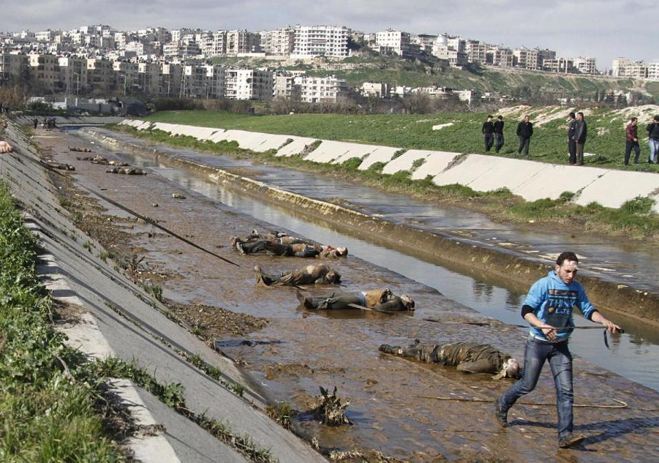 FILE - In this Jan. 29, 2013, file photo, a man walks past dead bodies in front of a river in the neighborhood of Bustan al-Qasr in Aleppo, Syria. The Britain-based Syrian Observatory for Human Rights said Tuesday that it has documented 150,344 deaths in the conflict that started in March 2011. The figure includes civilians, rebels, and members of the Syrian military. It also includes militiamen, fighting alongside President Bashar Assad’s forces and foreign fighters battling for Assad’s ouster on the rebels’ side. (AP Photo/Abdullah al-Yassin, File)