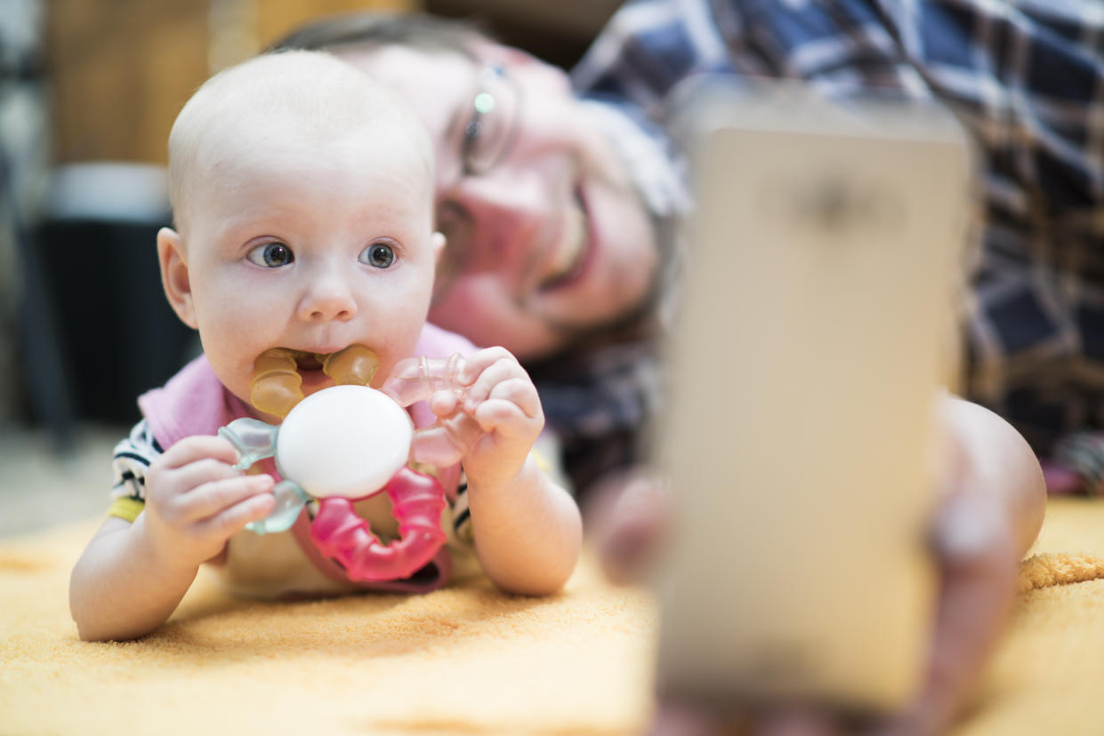 Young father with his baby daughter lying together on the floor and make selfie and have some video-conversation via the cellphone. Minsk, Belarus, Eastern Europe.