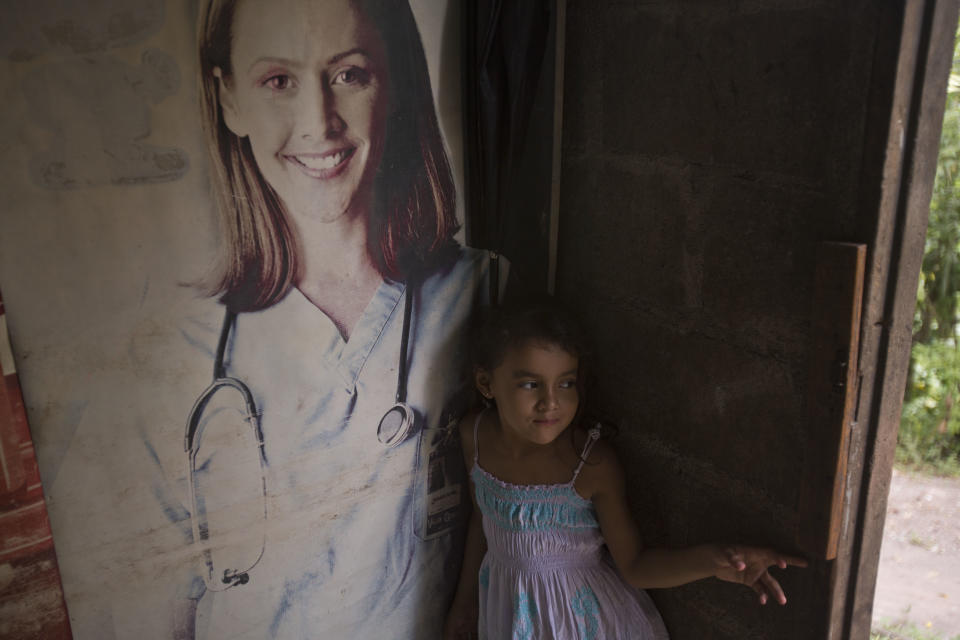 In this Nov. 2, 2018 photo, 5-year-old Janeisy Nicolle Cardona Orellana stands in her home where a metal advertisement featuring a doctor is used as a wall in San Pedro Sula, Honduras. Janeisy's parents are traveling to the U.S. border with a caravan of Central American migrants, hoping to reach the U.S. (AP Photo/Moises Castillo)