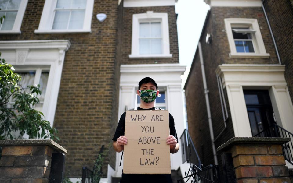 A protester holds up a placard which reads 'Why are you above the law?' outside the home of Dominic Cummings, Chief Advisor to Prime Minister Boris Johnson, on May 24, 2020 in London - GETTY IMAGES