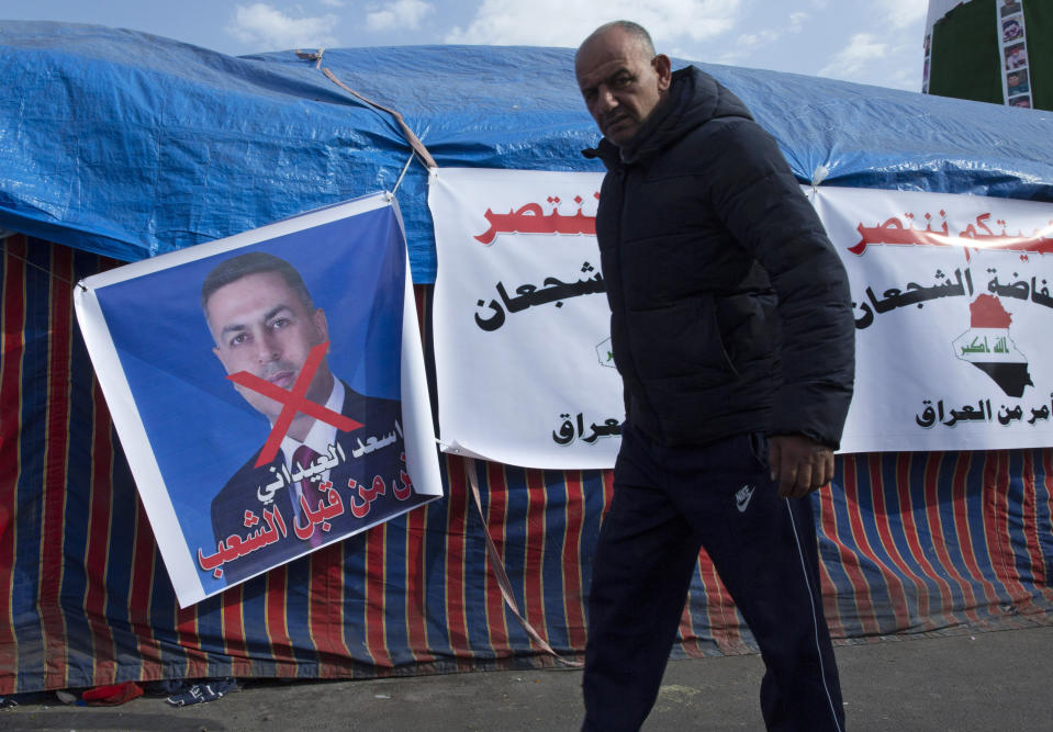 A protester walks past a poster with a defaced picture of the governor of the southern Basra province Asaad al-Eidani and Arabic that reads "rejected by the people," during the ongoing protests, in Tahrir square, in Baghdad, Iraq, Wednesday, Dec. 25, 2019. An Iranian-backed bloc in Iraq’s parliament proposed al-Eidani as the country’s next prime minister. However, the nomination was promptly rejected by Iraqi protesters who want an independent candidate to take over the government. Earlier on Wednesday, outgoing higher education minister, who had also been rejected by protesters on the streets, withdrew his nomination for prime minister. (AP Photo/Nasser Nasser)