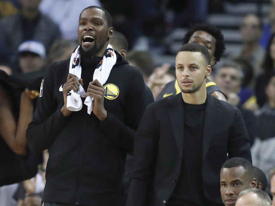 Golden State Warriors' Stephen Curry, right, and forward Kevin Durant watch from the bench during the second half of the team's NBA basketball game against the Portland Trail Blazers in Oakland, Calif., Friday, Nov. 23, 2018. The Warriors won 125-97. (AP Photo/Tony Avelar)