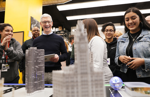 Apple CEO Tim Cook looks at a model cityscape with college-age students.