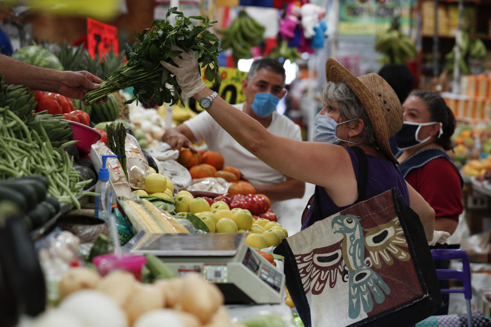 A shopper wearing a protective mask and gloves buys vegetables inside Mercado Medellin in the Roma Norte area of Mexico City, Thursday, April 2, 2020. Mexico has started taking tougher measures against the new coronavirus, but some experts warn the country is acting too late and testing too little to prevent the type of crisis unfolding across the border in the United States. (AP Photo/Rebecca Blackwell)