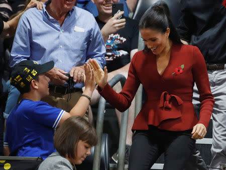 Meghan, Duchess of Sussex, gives a spectator a high five as she walks to her seat with Britain's Prince Harry (partially obscured) to watch the Invictus Games Sydney 2018 wheelchair basketball gold medal match at Quaycentre in Sydney, Australia October 27, 2018. REUTERS/Phil Noble