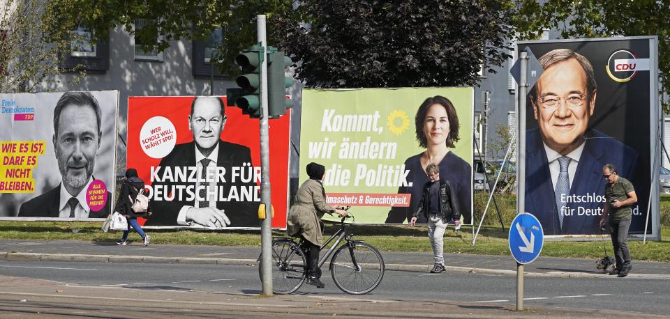 People walk and drive past election posters of the three chancellor candidates, from right, Armin Laschet, Christian Democratic Union (CDU), Annalena Baerbock, German Green party (Die Gruenen), Olaf Scholz, Social Democratic Party (SPD), and Christian Lindner, German Liberals (FDP) at a street in Gelsenkirchen, Germany, Thursday, Sept. 23, 2021 three days before the General election on Sunday, Sept. 26, 2021. (AP Photo/Martin Meissner)