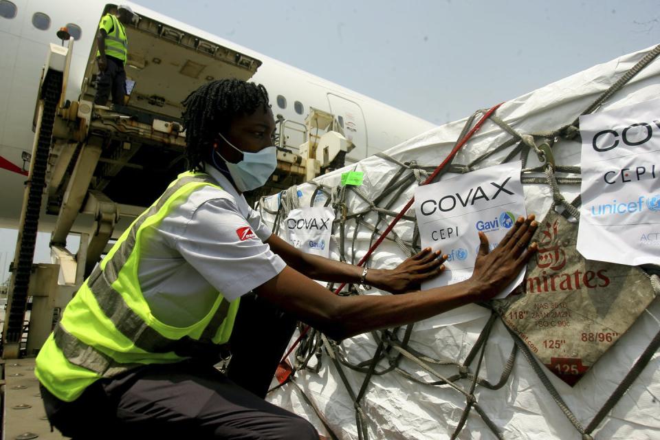 A person in a reflective vest and a face mask examining a crate with a COVAX label