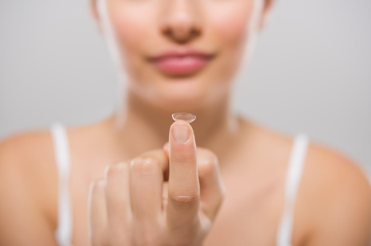 Focus on contact lens on finger of young woman. Young woman holding contact lens on finger in front of her face. Woman holding contact lens on grey background. Eyesight and eyecare concept.