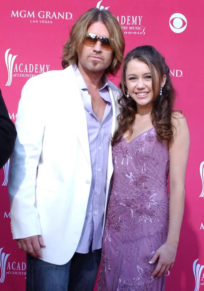 Billy Ray Cyrus in a white blazer and Miley Cyrus in a sequined dress pose together at the Academy of Country Music Awards