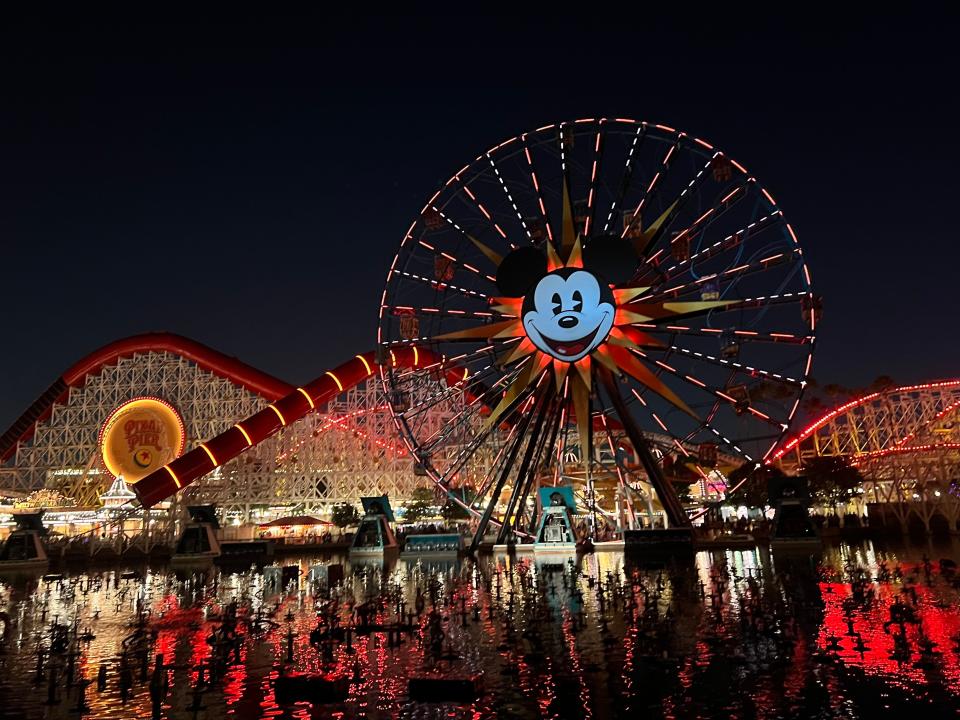 Disney California Adventure's Incredicoaster and iconic Pixar Pal-A-Round ferris wheel glow at night.