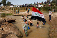 A boy holds the Iraqi flag as he plays in the water with other children during a Friday holiday at Shallalat district (Arabic for "waterfalls") in eastern Mosul, Iraq, April 21, 2017. REUTERS/Muhammad Hamed