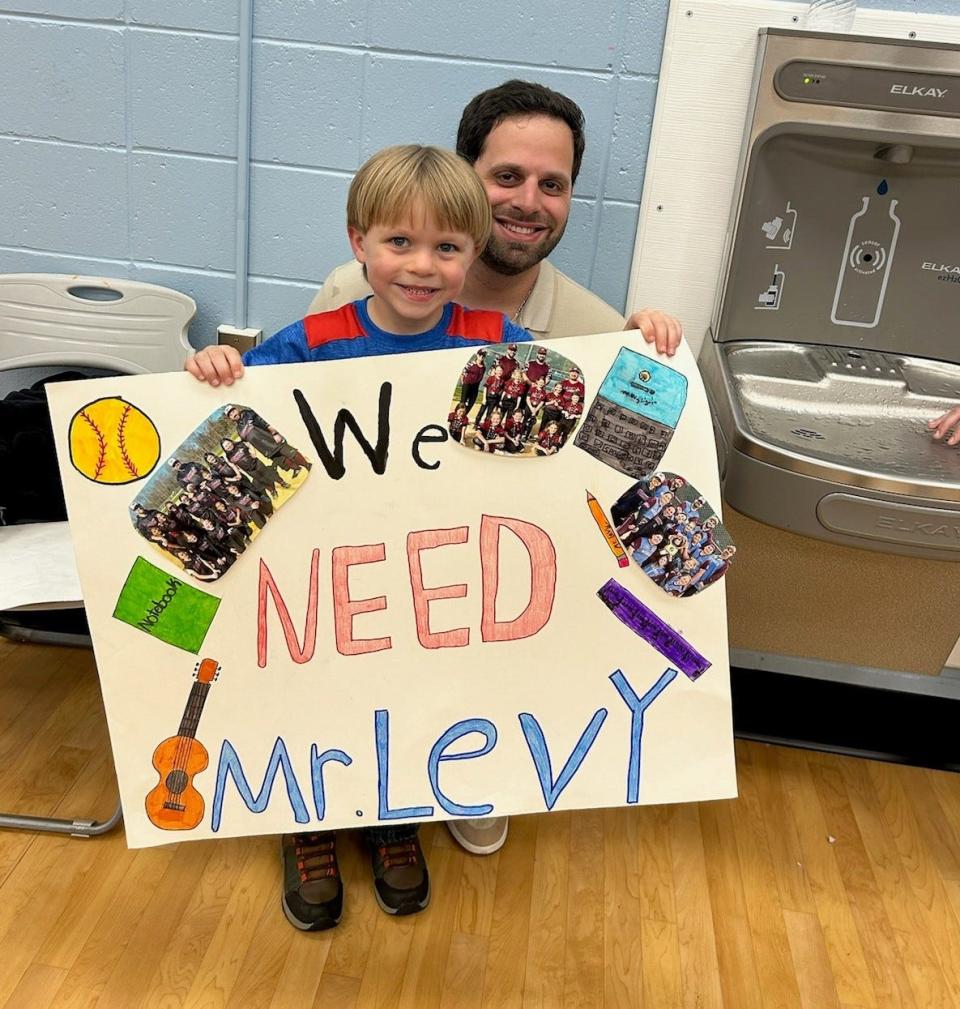 Alexander Allen, a student at Strathmore Elementary School in Aberdeen, holds a sign in support of third-grade teacher Josh Levy, seen crouching behind him.
